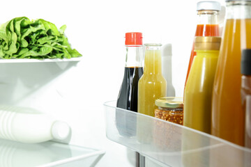 Bottles with different tasty sauces and products in fridge, closeup