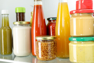 Bottles with different tasty sauces in fridge, closeup