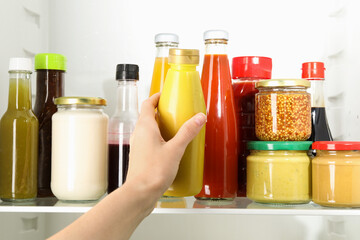 Woman taking bottle of tasty mustard sauce from fridge, closeup