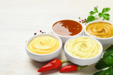 Different tasty sauces in bowls, parsley, peppercorns and chili peppers on white wooden table, closeup. Space for text
