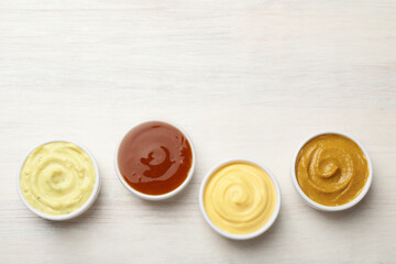 Different tasty sauces in bowls on white wooden table, flat lay. Space for text