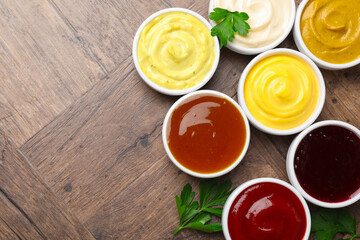 Different tasty sauces in bowls and parsley on wooden table, flat lay. Space for text