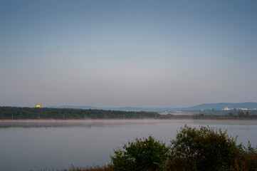 The sun sets over a beautiful lake, with a settlement visible in the background.