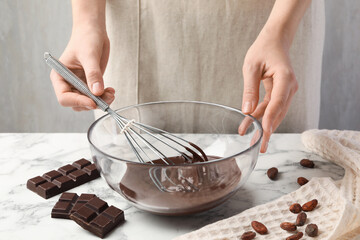 Woman mixing melted chocolate in bowl at white table, closeup