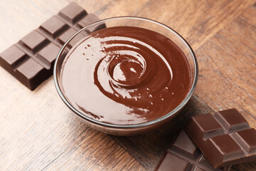 Bowl with melted chocolate and pieces on wooden table, closeup