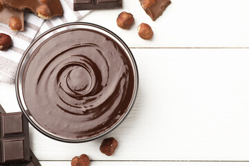 Melted chocolate and pieces with hazelnuts on white wooden table, flat lay. Space for text