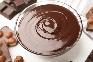 Melted chocolate and pieces with hazelnuts on white wooden table, closeup