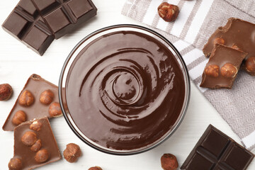 Melted chocolate and pieces with hazelnuts on white wooden table, flat lay