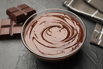 Bowl with melted chocolate and pieces on black table, closeup