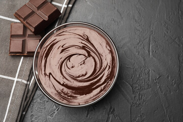 Bowl with melted chocolate and pieces on black table, flat lay. Space for text