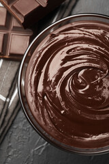 Bowl with melted chocolate and pieces on black table, top view