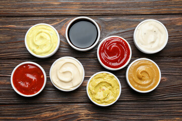 Different sauces in bowls on wooden table, flat lay