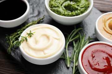 Different sauces and herbs on wooden table, closeup