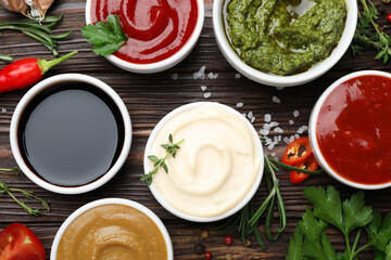 Different sauces, spices and herbs on wooden table, flat lay