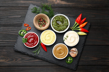 Different sauces and herbs on wooden table, flat lay