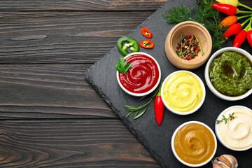 Different sauces and herbs on wooden table, flat lay. Space for text