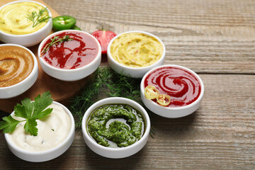 Different sauces and herbs on wooden table, closeup. Space for text