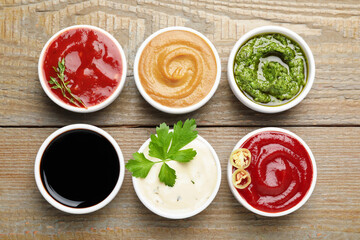 Different sauces and herbs on wooden table, flat lay