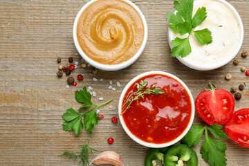 Different sauces, spices and parsley on wooden table, flat lay