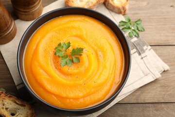 Tasty pumpkin cream soup with spices in bowl on wooden table, above view
