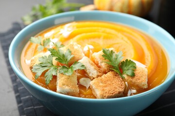 Tasty pumpkin cream soup with parsley and croutons in bowl on table, closeup