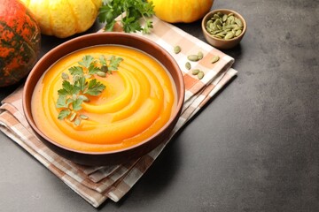 Tasty pumpkin cream soup with parsley and seeds in bowl on gray textured table, closeup. Space for text