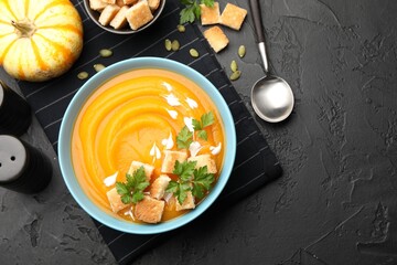 Tasty pumpkin cream soup with parsley and croutons served on dark textured table, flat lay. Space for text