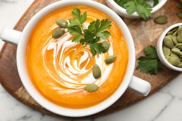Tasty pumpkin cream soup with parsley and seeds in bowl on table, flat lay