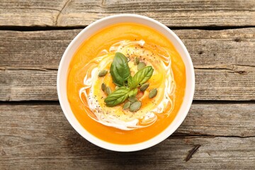 Delicious pumpkin cream soup with basil and seeds served on wooden table, top view