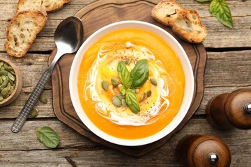 Delicious pumpkin cream soup with basil and seeds served on wooden table, flat lay