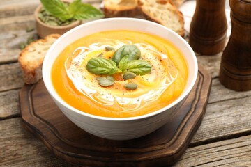 Delicious pumpkin cream soup with basil and seeds served on wooden table, closeup