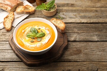Delicious pumpkin cream soup with basil and seeds served on wooden table. Space for text