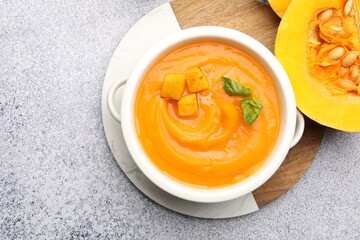 Delicious pumpkin cream soup with basil served on grey table, top view