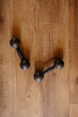 Two black dumbbells for sports lying on a wooden floor, filmed from above