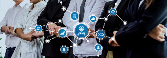 A professional business team is engaged in a collaborative discussion, focusing on CRM strategies, showcased through digital icons and modern technology elements in an office setting. Amity