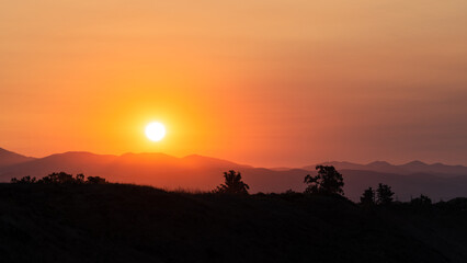 bright orange sunrise over silhouette of trees and hills
