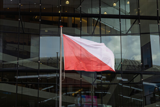 Dutch provincial flag of Utrecht, featuring a white and red diagonal cross, waving on a flagpole against a modern glass office building facade.
