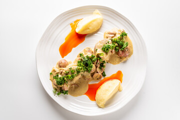 gourmet dish featuring sliced chicken or pork with a creamy mushroom sauce and fresh herbs, served with a side of mashed potatoes on a white plate.