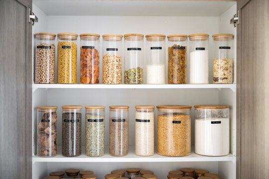 Neatly organized labeled food pantry in a home kitchen with spices grains flour rice sugar nuts