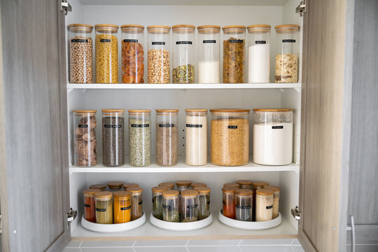 Neatly organized labeled food pantry in a home kitchen with spices grains flour rice sugar nuts
