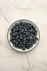 Plate with blueberries on white marble background