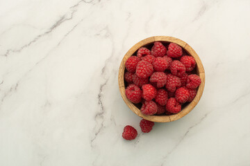 Raspberries in a wooden plate on a white marble background