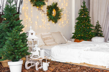 Bright cozy bedroom interior with Christmas trees, wreaths, and fairy lights. Warm festive atmosphere with bed with white bedding and decorative pillows, candles, and natural wooden decor elements.
