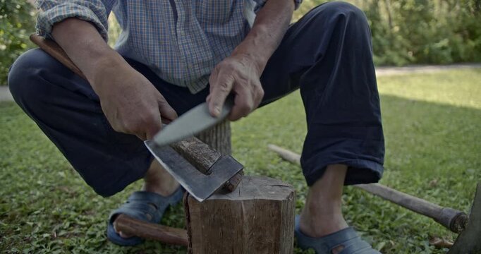 Experience the authentic sounds of manual labor as a man sharpens an axe with a whetstone outdoors. This video captures the traditional craft and meticulous process.