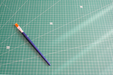 Single blue and orange paintbrush lying diagonally across a green cutting mat with a precise grid pattern providing generous copy space a clean concept for art design or education