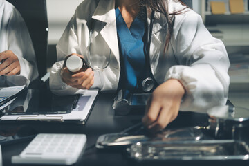 Two doctors and a female nurse meet at a table in the hospital, collaborating on medical tasks using laptops and computers