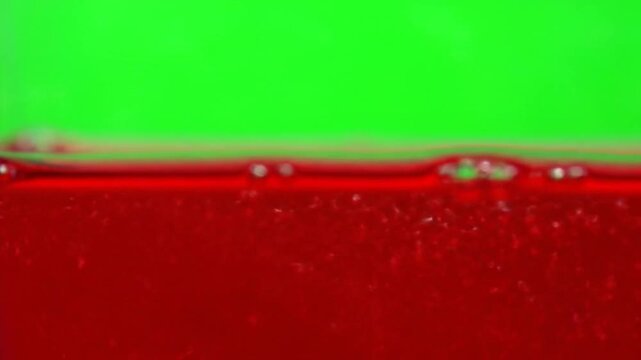 Vibrant red liquid with subtle bubbles flowing against a bright green background