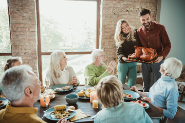 Family gathers for a festive Thanksgiving feast as a couple presents a roasted turkey to delighted...