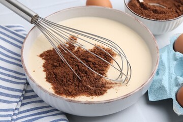 Adding cocoa powder into bowl with dough at white table, closeup