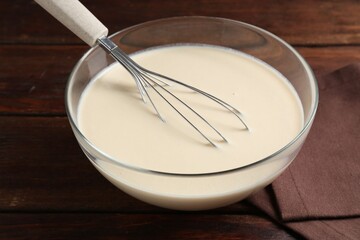 Liquid dough in bowl and whisk on wooden table, closeup